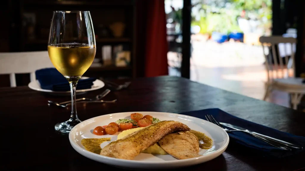 Plato fuerte de pescado junto con una copa de vino blanco